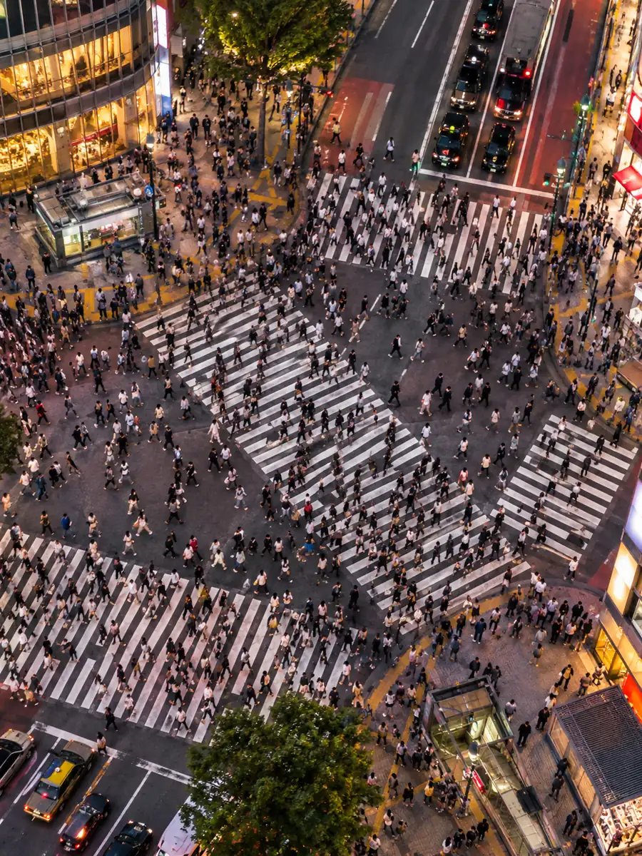 夕方早い時間の渋谷スクランブル交差点を真上から見下ろした様子。何百人もの人が白い横断歩道をあらゆる方向に渡っている