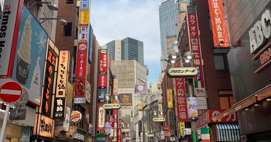 晴れた日の渋谷のにぎやかな商店街。店の看板と高いビルが並んでいます